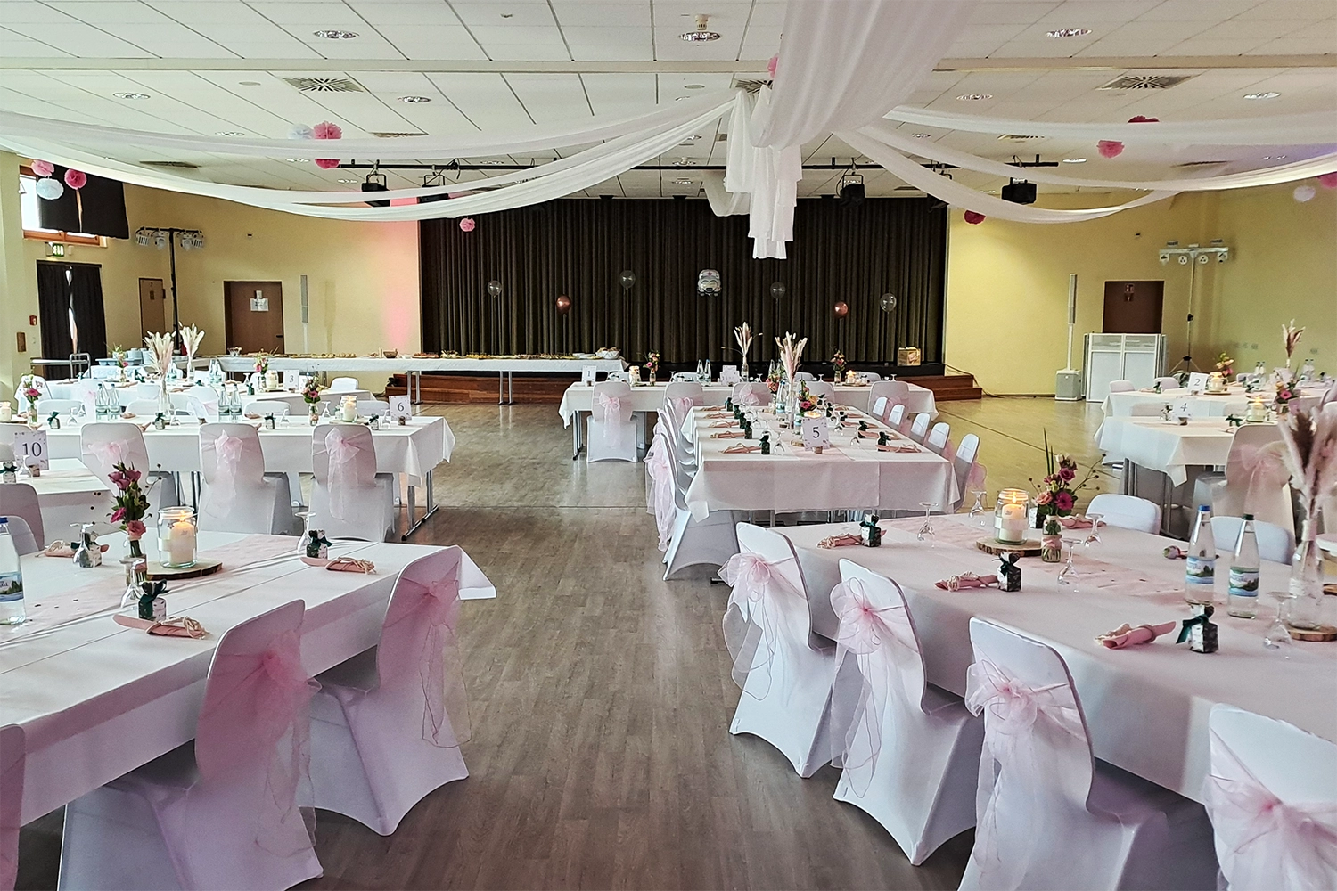 Festlich dekorierter Hochzeitssaal in Neustadt an der Aisch mit weißen Hussen über Tischen und Stühlen.